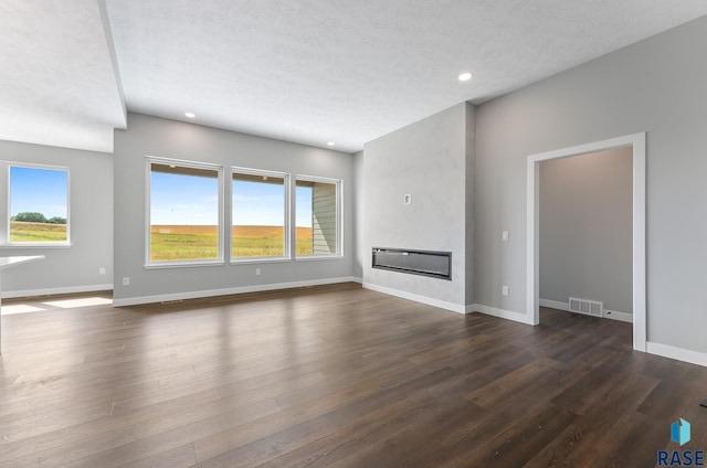 unfurnished living room with dark wood-style flooring, a glass covered fireplace, visible vents, and baseboards