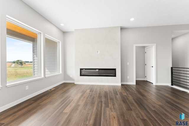 unfurnished living room with a large fireplace, dark wood-style flooring, and baseboards