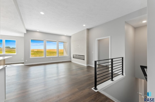 living area featuring a healthy amount of sunlight, baseboards, dark wood-style flooring, and a glass covered fireplace