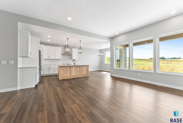 kitchen featuring dark wood-style floors, open floor plan, a chandelier, wall chimney exhaust hood, and stainless steel refrigerator