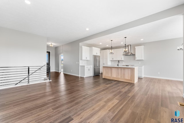 kitchen featuring wall chimney exhaust hood, light countertops, open floor plan, a sink, and high end refrigerator