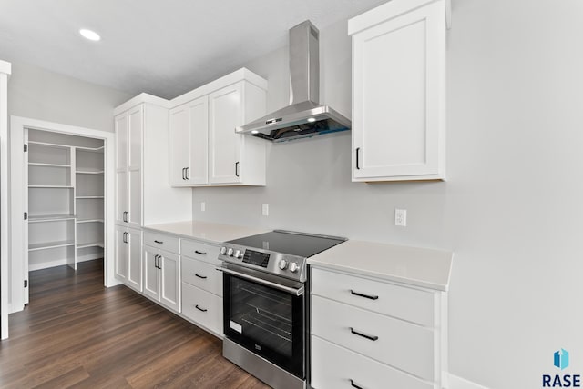 kitchen featuring wall chimney exhaust hood, dark wood-type flooring, light countertops, and stainless steel range with electric stovetop