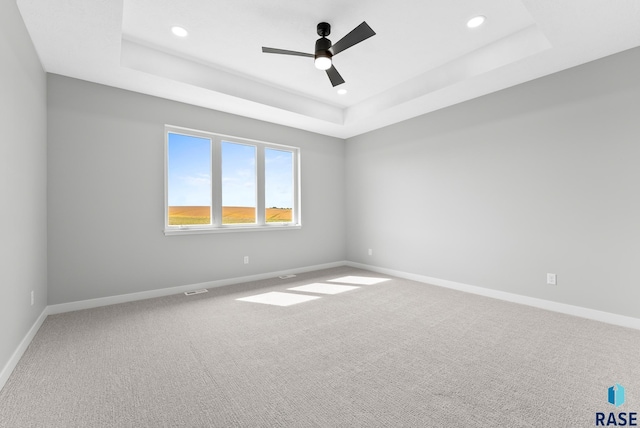 empty room featuring carpet floors, a raised ceiling, and baseboards