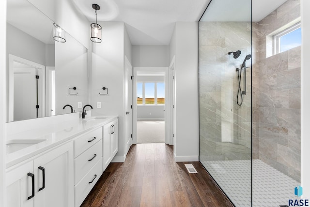 full bath featuring double vanity, visible vents, wood finished floors, a walk in shower, and a sink