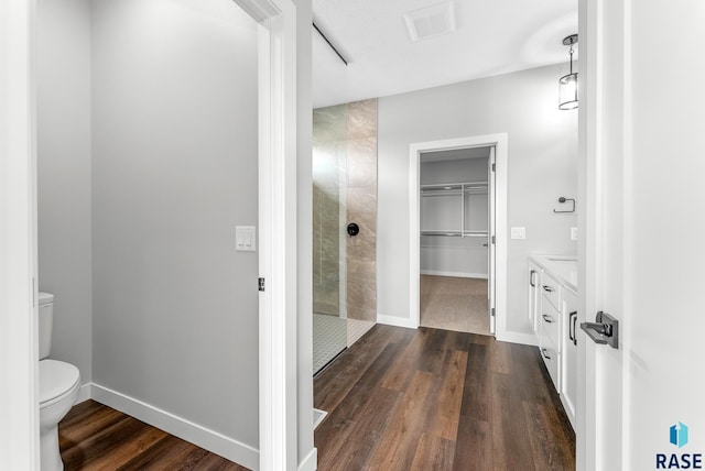 full bath with tiled shower, wood finished floors, toilet, and baseboards