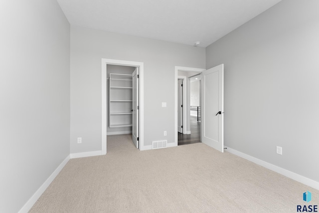 unfurnished bedroom featuring carpet floors, a walk in closet, a closet, visible vents, and baseboards