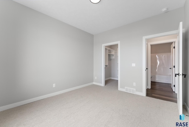 unfurnished bedroom with carpet floors, a walk in closet, a closet, visible vents, and baseboards