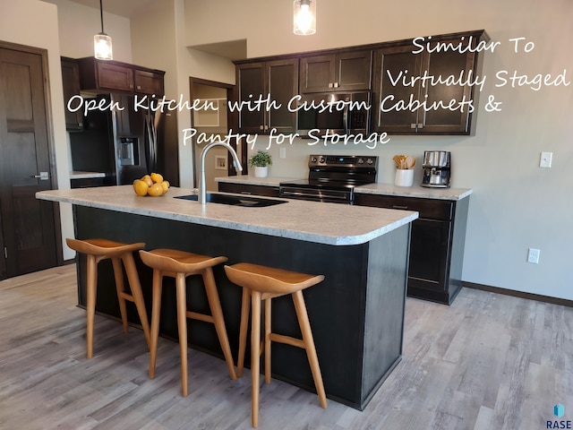 kitchen featuring a center island with sink, range with electric cooktop, a sink, light countertops, and black fridge