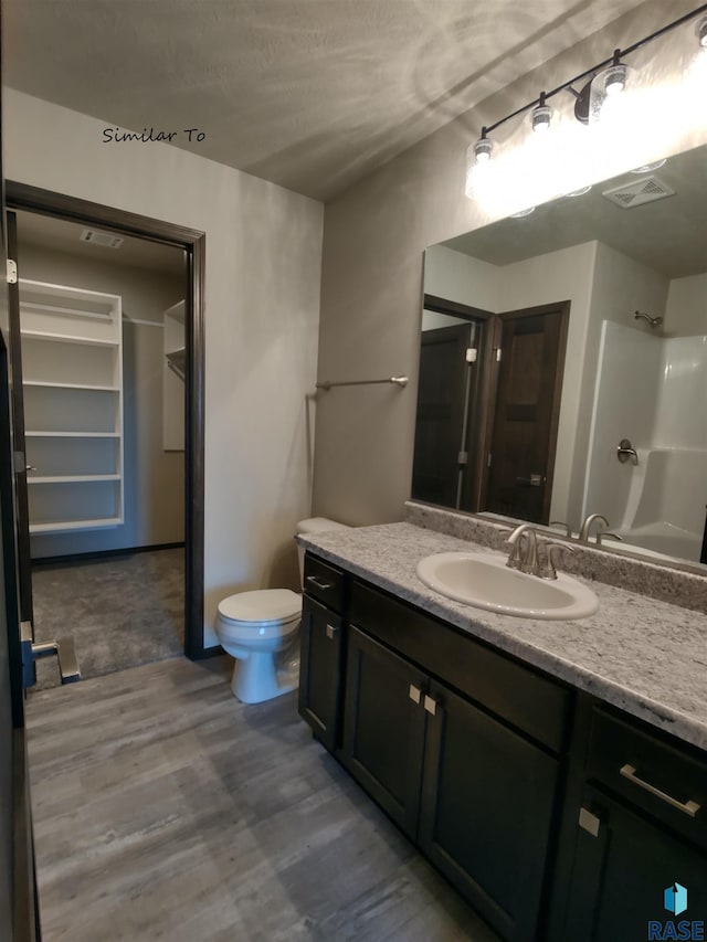 full bathroom featuring toilet, wood finished floors, vanity, visible vents, and a shower