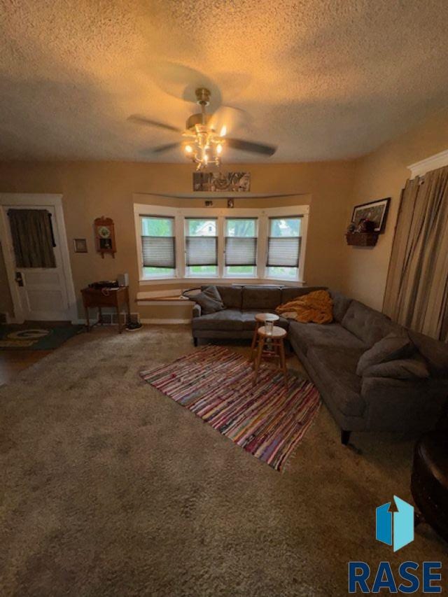 carpeted living room featuring ceiling fan and a textured ceiling