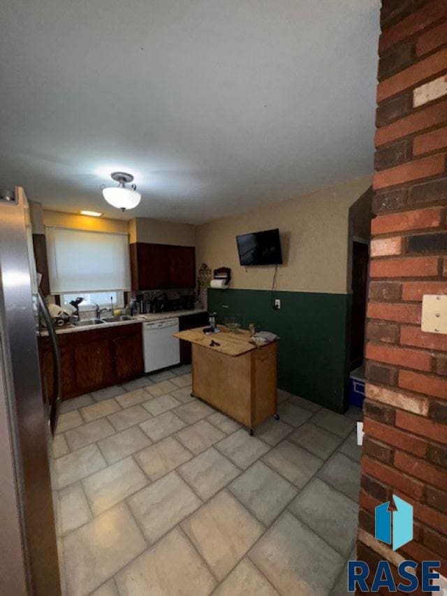 kitchen with light tile patterned floors, dishwasher, a center island, brick wall, and stainless steel fridge