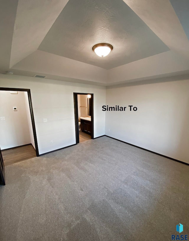 unfurnished bedroom featuring a textured ceiling, carpet flooring, a raised ceiling, and ensuite bath