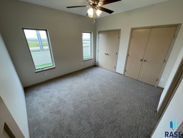 unfurnished bedroom with light carpet, multiple closets, ceiling fan, and multiple windows