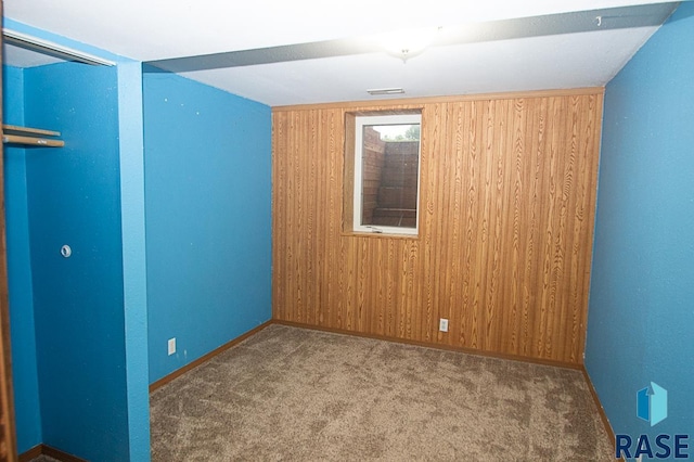 unfurnished room featuring carpet, wooden walls, visible vents, and baseboards