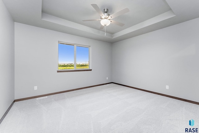 spare room with ceiling fan, a raised ceiling, and carpet floors