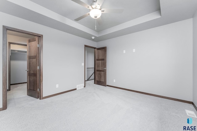 unfurnished bedroom with a tray ceiling, ceiling fan, and light carpet