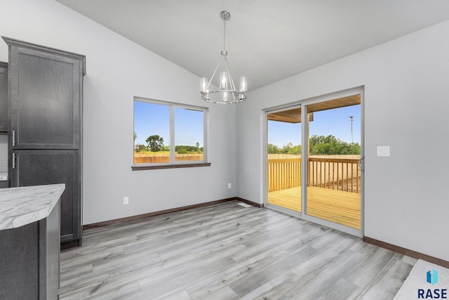 unfurnished dining area featuring light wood-type flooring, a chandelier, and lofted ceiling