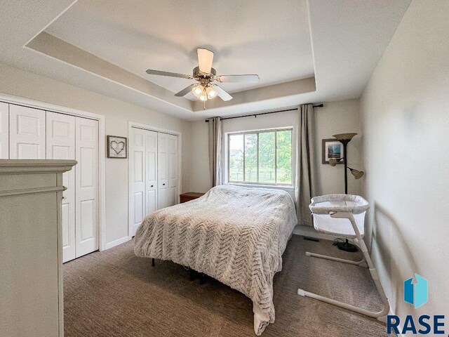 bedroom with carpet, a raised ceiling, two closets, and ceiling fan