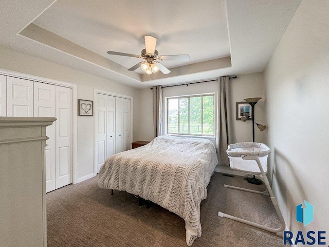 carpeted bedroom with a tray ceiling, two closets, and ceiling fan