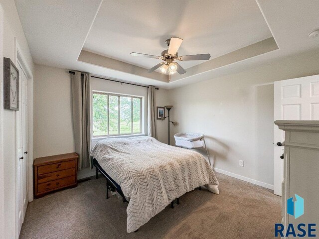 bedroom with ceiling fan, a raised ceiling, and light carpet