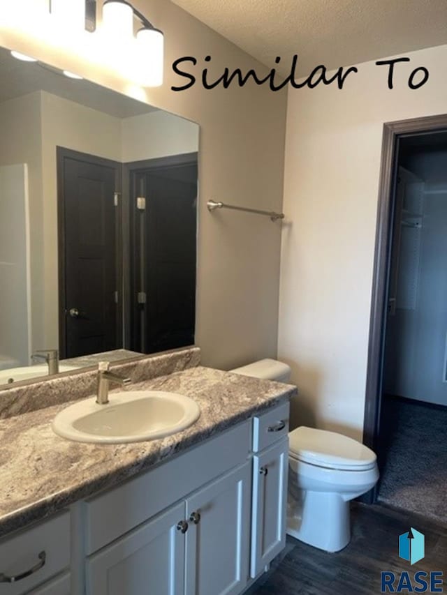 full bathroom featuring a textured ceiling, toilet, wood finished floors, and vanity