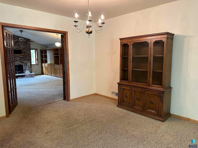 unfurnished dining area featuring brick wall, a fireplace, lofted ceiling, light colored carpet, and a notable chandelier