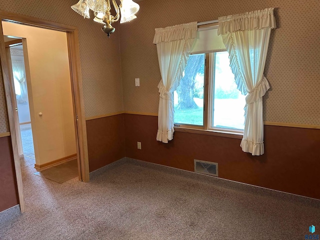 carpeted spare room featuring an inviting chandelier