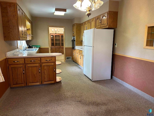 kitchen featuring an inviting chandelier, black oven, sink, kitchen peninsula, and white fridge