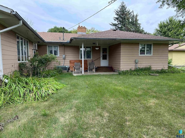 rear view of house with central AC unit and a lawn