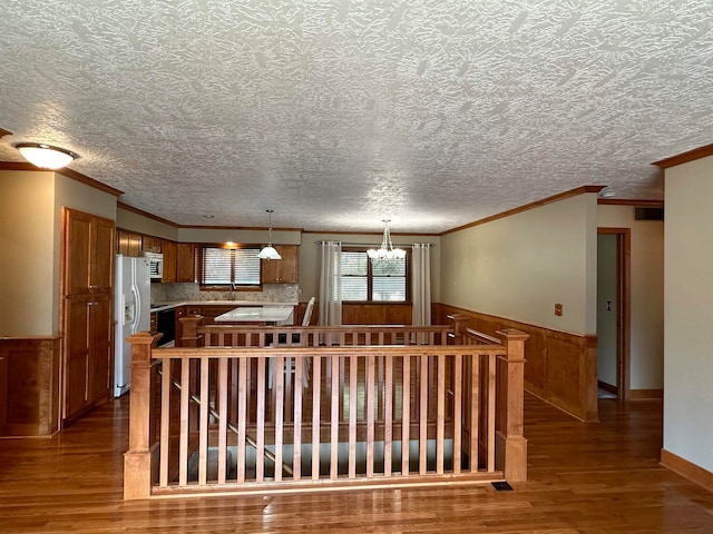 kitchen with a textured ceiling, pendant lighting, ornamental molding, and wood-type flooring