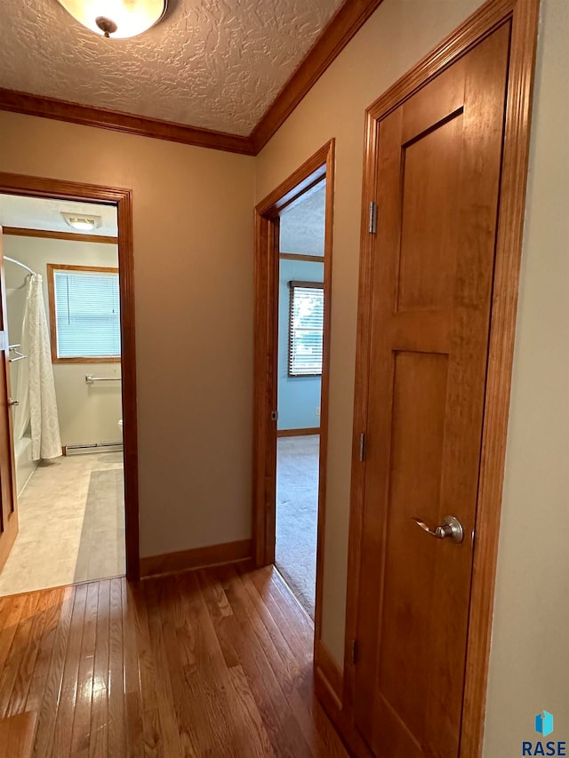 hallway with a textured ceiling, ornamental molding, and light wood-type flooring