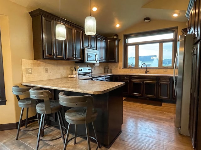 kitchen with decorative backsplash, light hardwood / wood-style flooring, kitchen peninsula, lofted ceiling, and stainless steel appliances