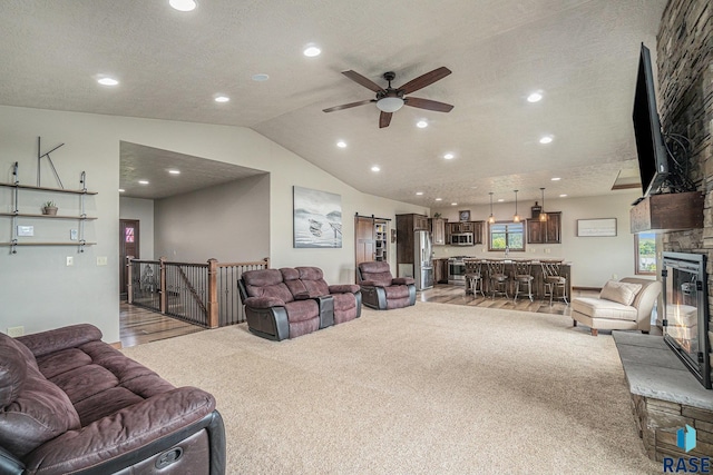 carpeted living room with ceiling fan, a stone fireplace, and a textured ceiling