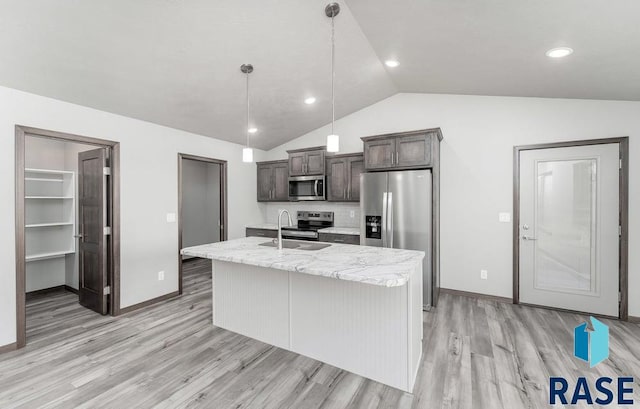 kitchen with lofted ceiling, a center island with sink, appliances with stainless steel finishes, sink, and decorative light fixtures