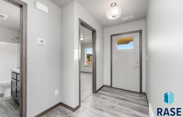 doorway with baseboards, light wood finished floors, and visible vents