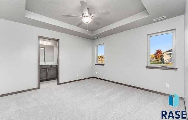 unfurnished bedroom featuring light carpet, ensuite bath, sink, a raised ceiling, and ceiling fan