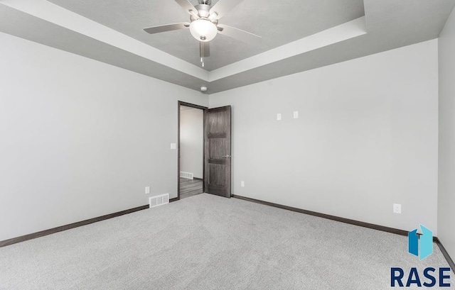 carpeted empty room featuring ceiling fan and a raised ceiling