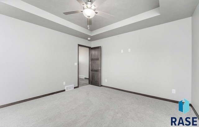carpeted spare room with visible vents, a raised ceiling, baseboards, and a ceiling fan