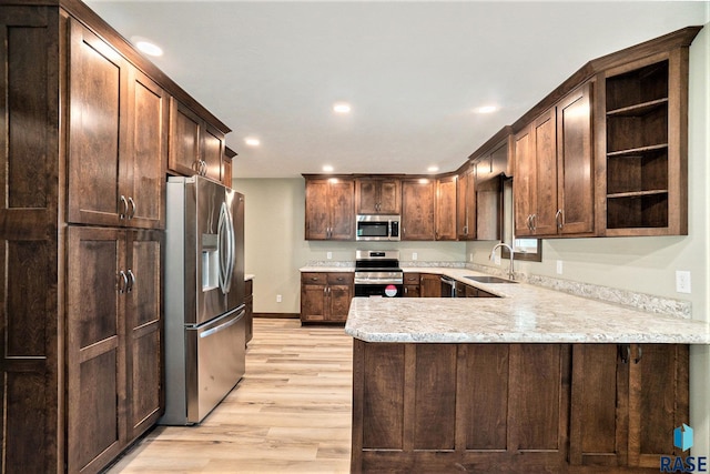 kitchen featuring open shelves, appliances with stainless steel finishes, a sink, light wood-type flooring, and a peninsula