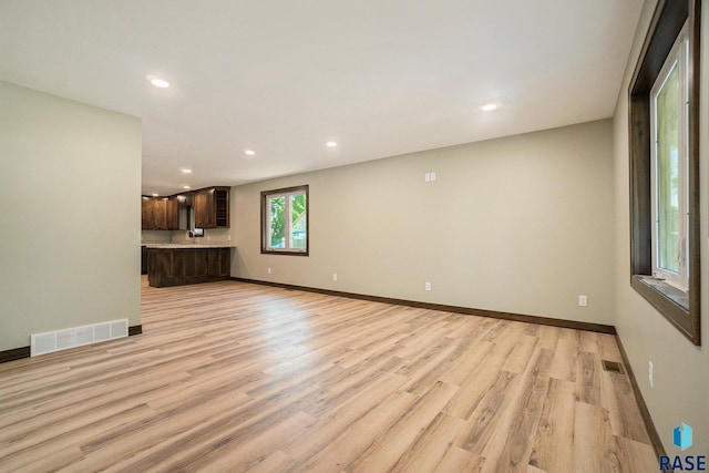 unfurnished living room with light wood-type flooring, baseboards, and visible vents