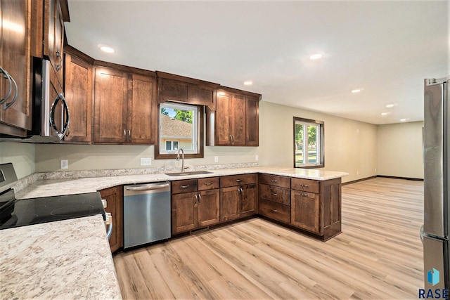 kitchen with appliances with stainless steel finishes, light wood-style floors, a sink, and a peninsula