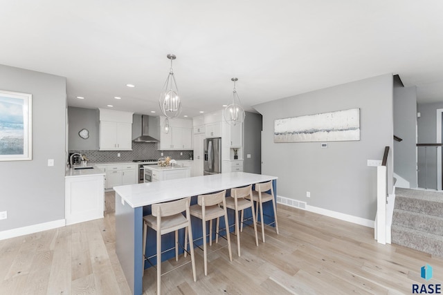 kitchen with white cabinets, stainless steel fridge with ice dispenser, a kitchen island, light countertops, and wall chimney range hood