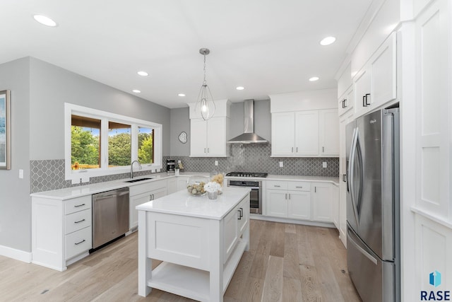 kitchen with decorative light fixtures, stainless steel appliances, a sink, wall chimney range hood, and a kitchen island