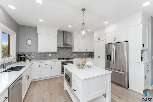 kitchen featuring a kitchen island, hanging light fixtures, stainless steel appliances, wall chimney range hood, and a sink