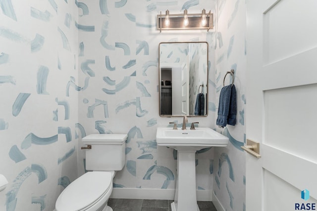 half bath with baseboards, a sink, toilet, and wallpapered walls