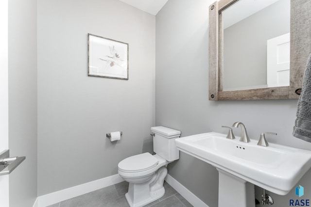 half bath with a sink, tile patterned flooring, toilet, and baseboards