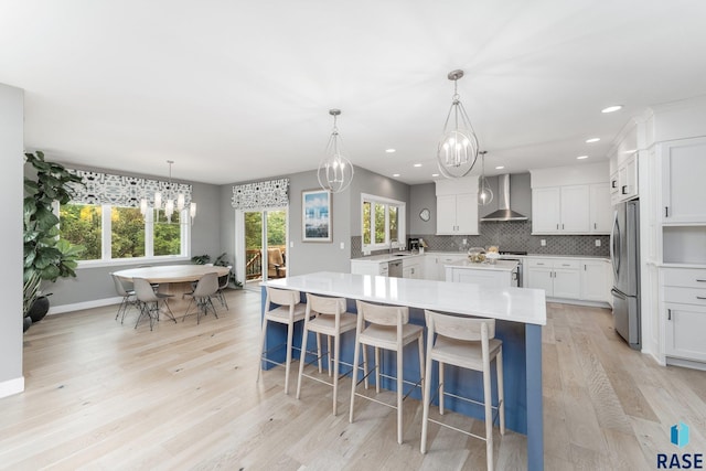 kitchen with light countertops, an inviting chandelier, appliances with stainless steel finishes, white cabinets, and wall chimney range hood