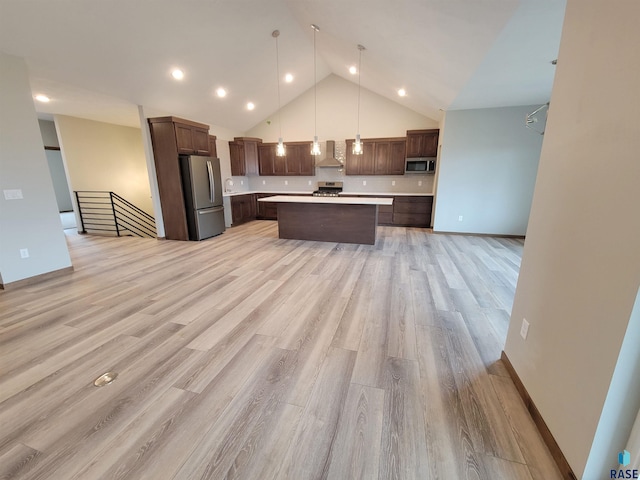 kitchen with light countertops, appliances with stainless steel finishes, a kitchen island, high vaulted ceiling, and wall chimney exhaust hood