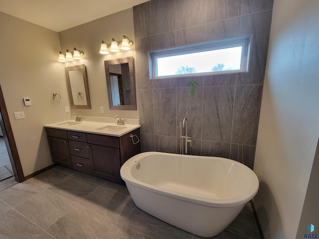 full bathroom featuring double vanity, a freestanding tub, tile walls, and a sink