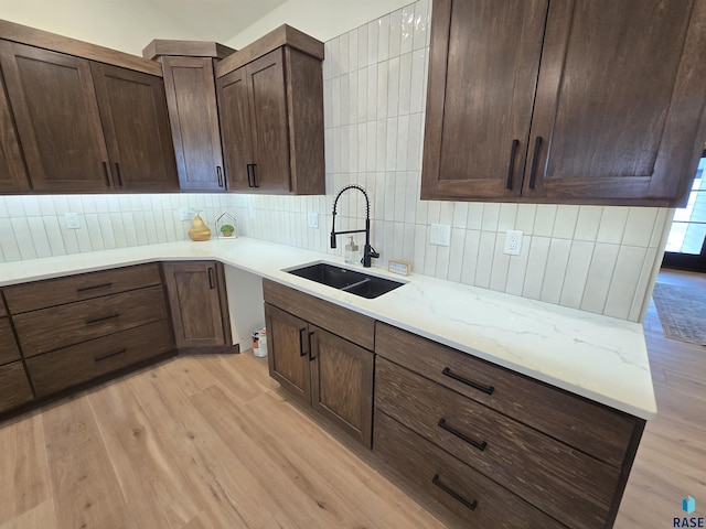 8106 E Norway Pines Trl, Sioux Falls, SD 57110 - kitchen featuring light wood-style flooring, dark brown cabinetry, a sink, light stone counters, and backsplash
